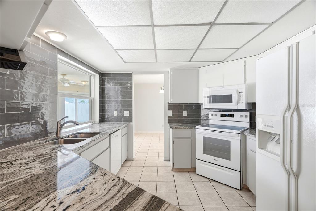 A kitchen with gray subway tile backsplash, granite countertops, white appliances, and a drop ceiling — 13219 RIDGE ROAD, LARGO, FL