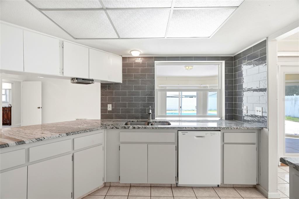 A kitchen features white cabinets, granite countertops, gray subway tile backsplash, and a white dishwasher — 13219 RIDGE ROAD, LARGO, FL