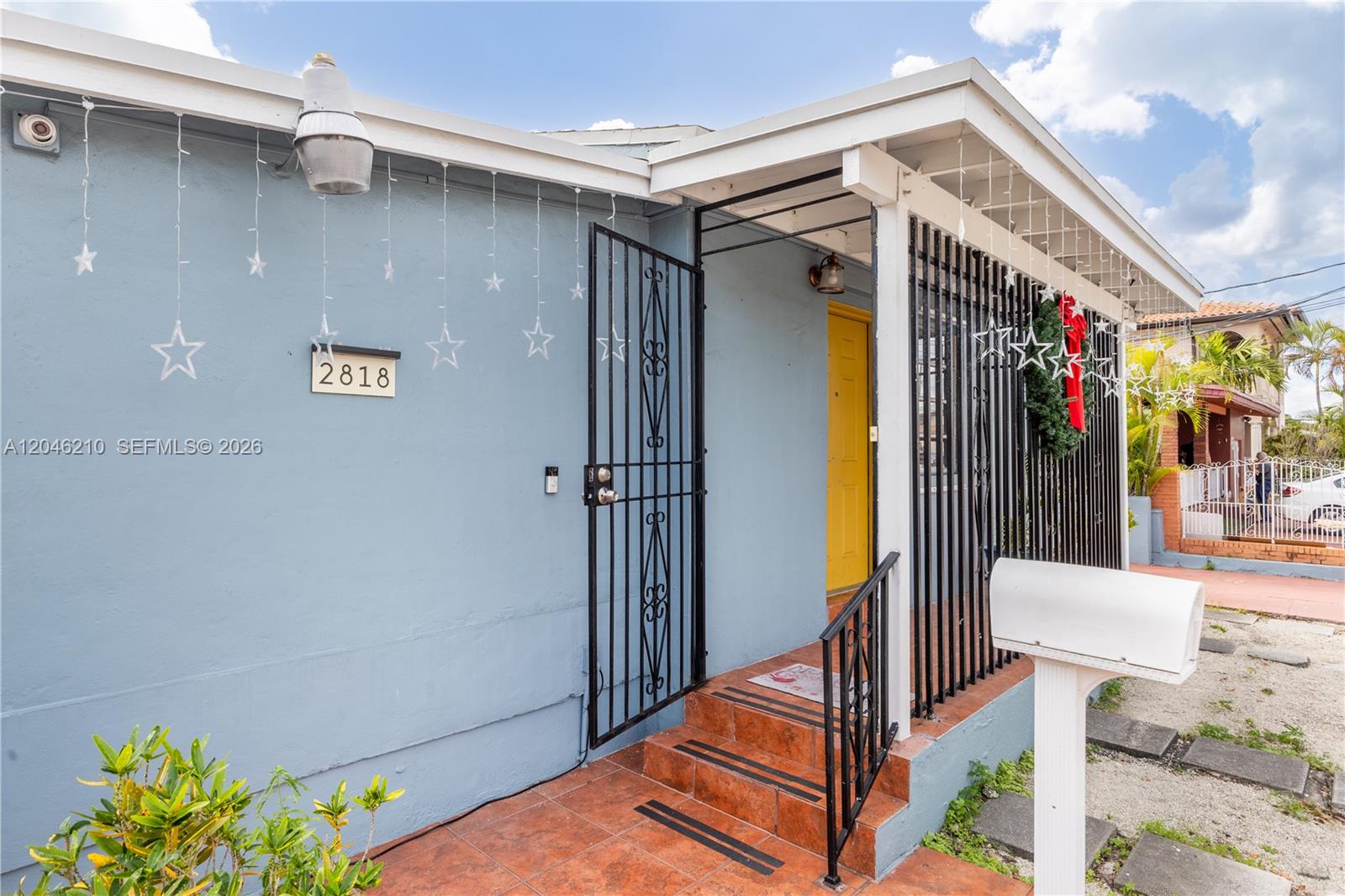 The exterior of a light blue house features a yellow door, security gate, and stairs — 2818 SW 2nd St, Miami FL 33135, MIAMI, FL