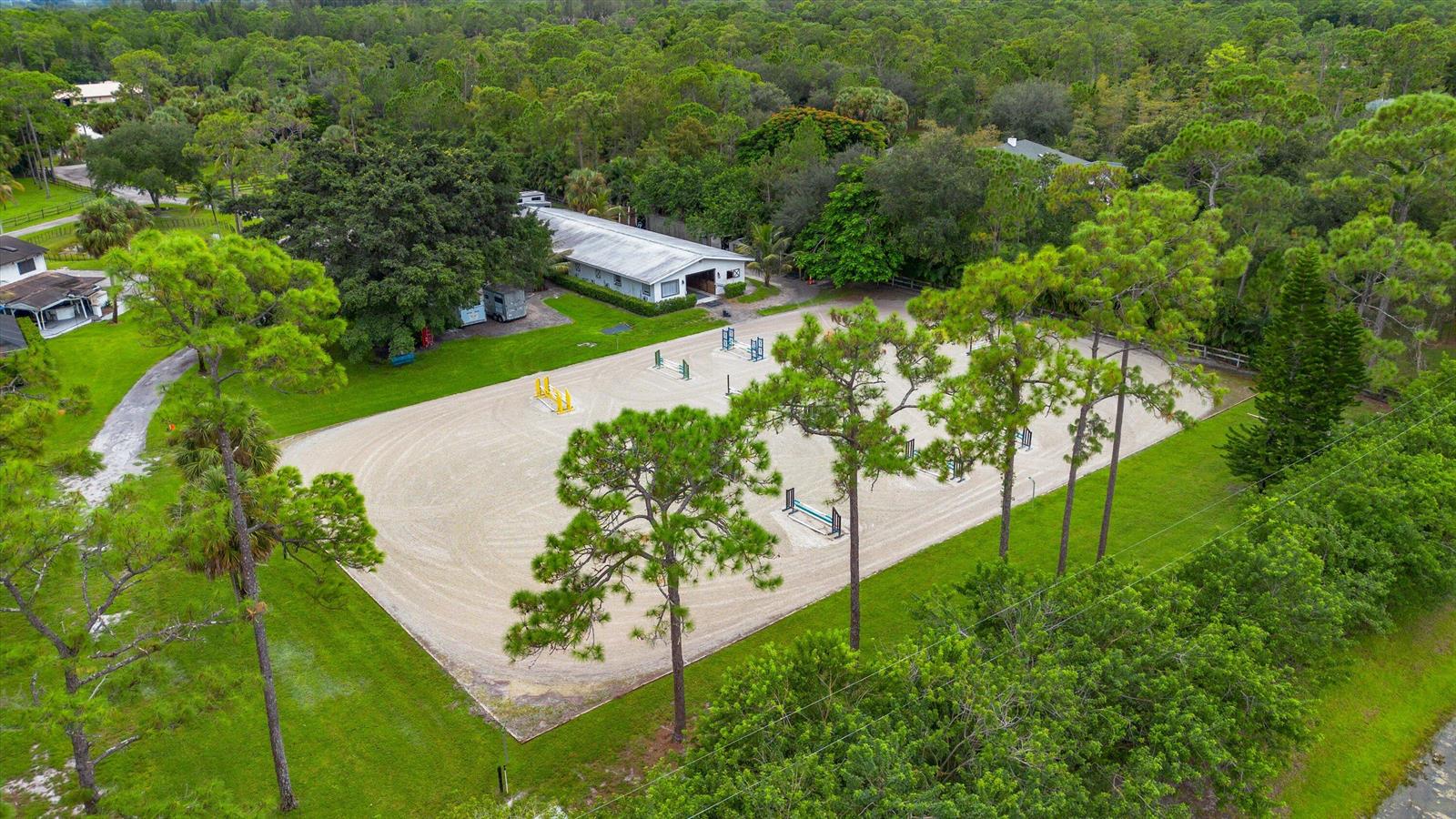 An aerial view of a sandy equestrian riding arena surrounded by trees and a stable — 2915 Doe Trail, FL 33470, FL