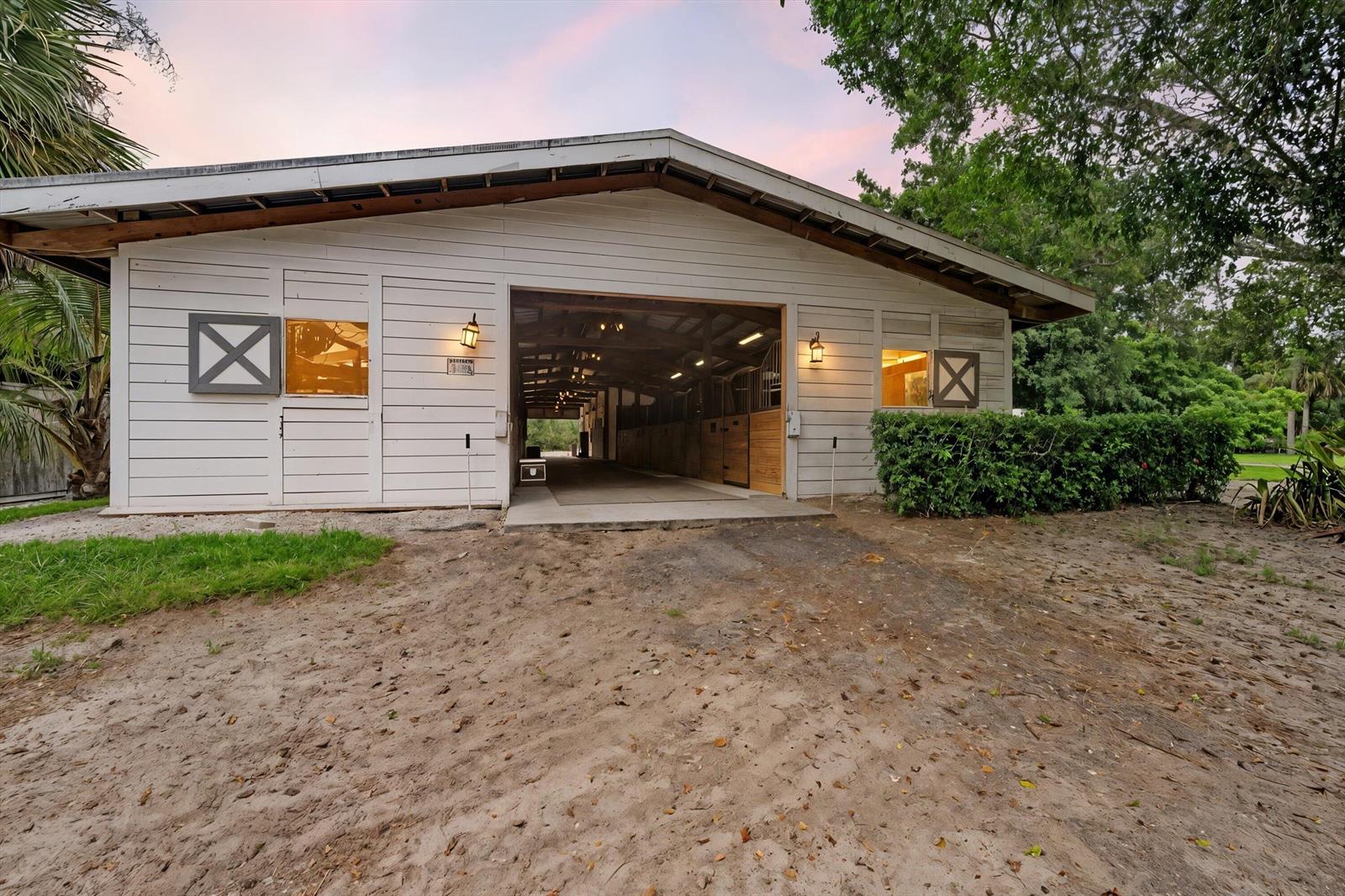 A white wooden horse barn with an open center aisle and exterior wall-mounted lanterns — 2915 Doe Trail, FL 33470, FL