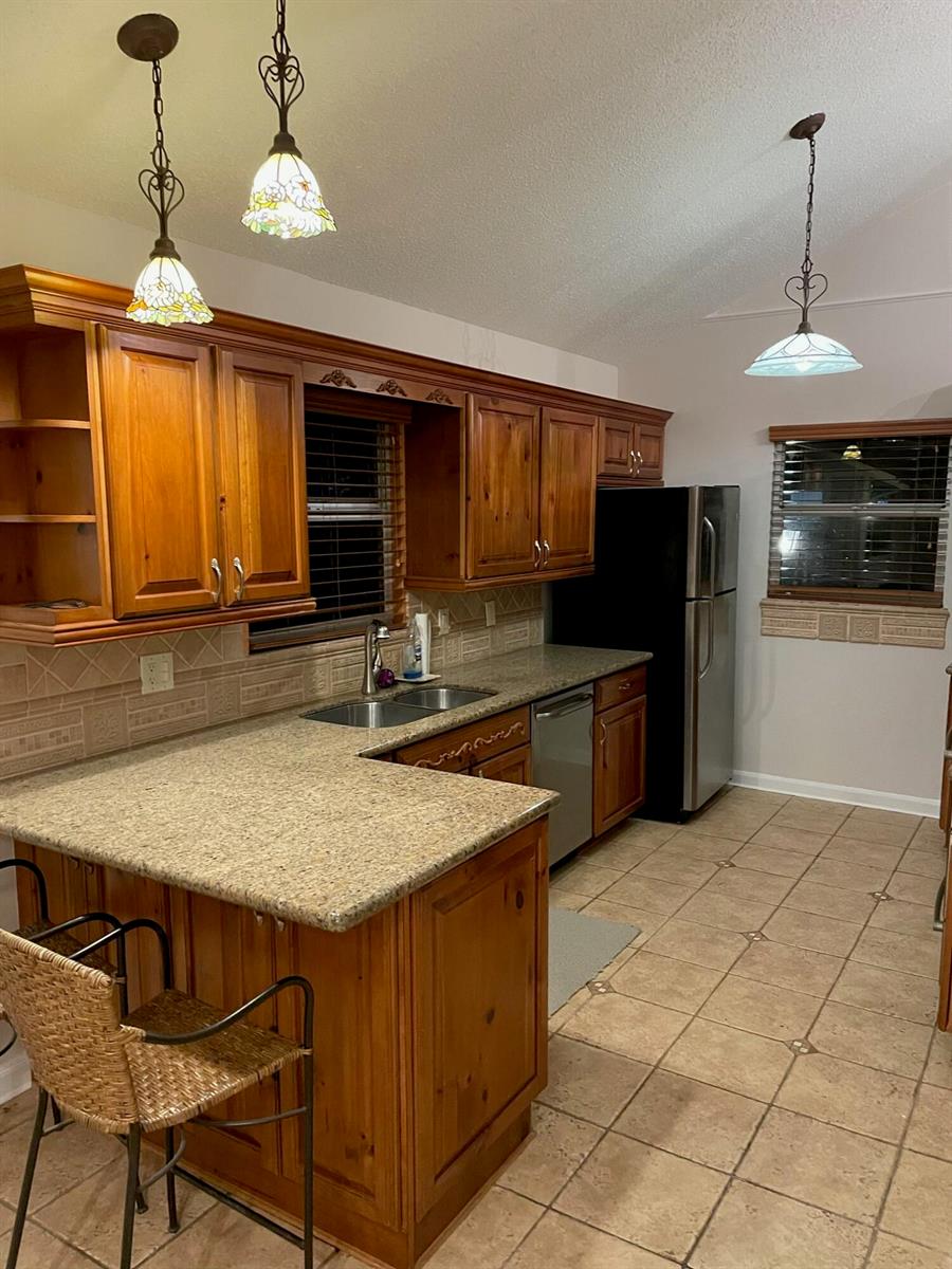A kitchen features wood cabinets, granite countertops, tile flooring, and three hanging pendant lights — 232 Maplecrest Circle, Jupiter FL 33458, JUPITER, FL