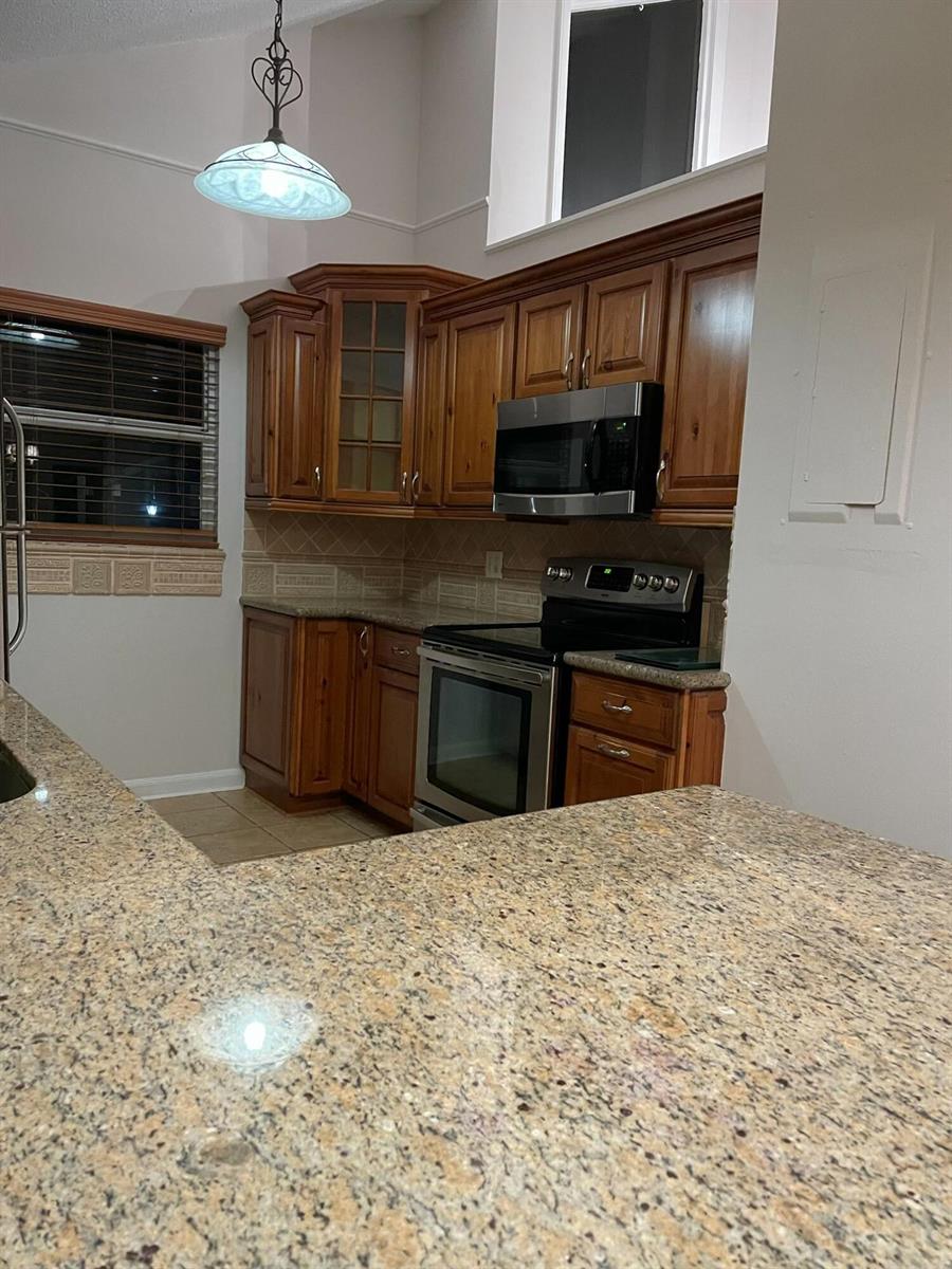 A kitchen features wood cabinets, granite countertops, stainless steel appliances, and a pendant light — 232 Maplecrest Circle, Jupiter FL 33458, JUPITER, FL