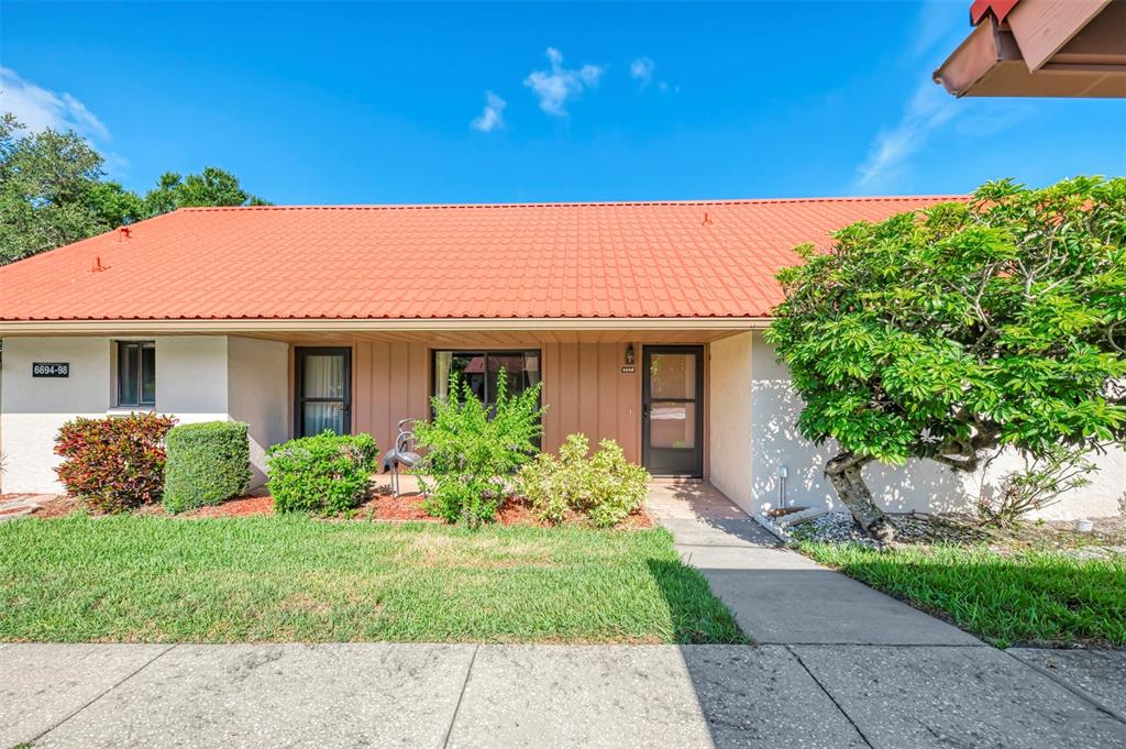 A single-story building with a red metal roof, tan siding, and a front walkway — 6698 DRAW LANE UNIT 140, SARASOTA, FL