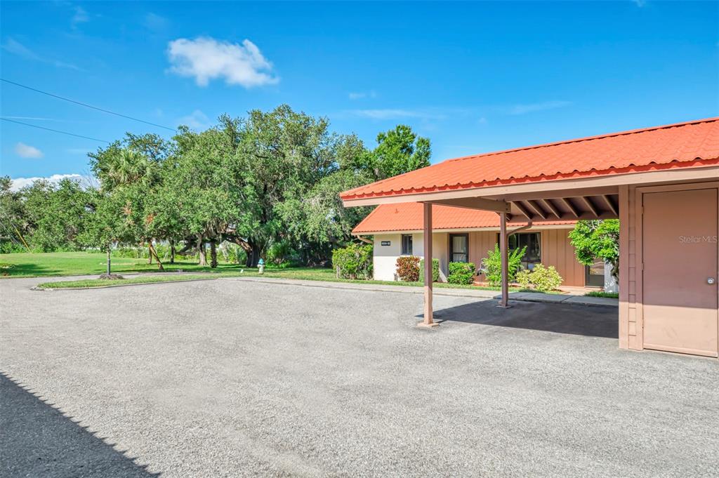 A gravel parking area sits in front of a building with a covered carport — 6698 DRAW LANE UNIT 140, SARASOTA, FL