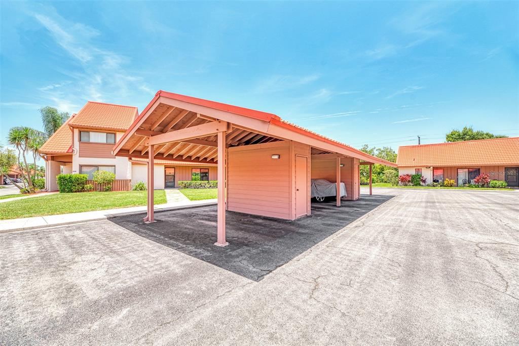 A pink-toned carport structure stands in a paved parking lot near residential buildings — 6698 DRAW LANE UNIT 140, SARASOTA, FL