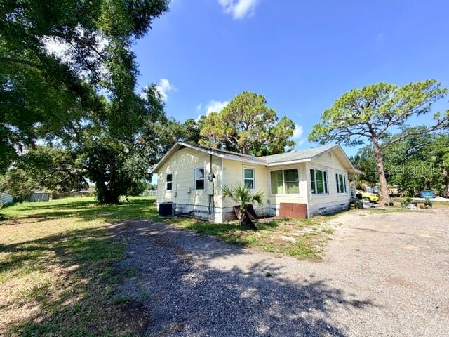 A light yellow single-story house sits on a gravel lot surrounded by large trees — 420 53RD AVENUE E, BRADENTON, FL