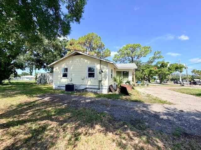 A light yellow, single-story house with a gravel driveway and surrounding trees — 420 53RD AVENUE E, BRADENTON, FL