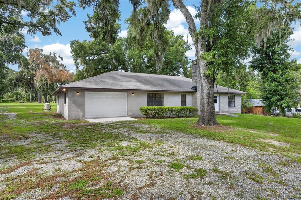 A single-story house with a white garage door, gray siding, and a gravel driveway — 615 THOMPSON ROAD, LITHIA, FL