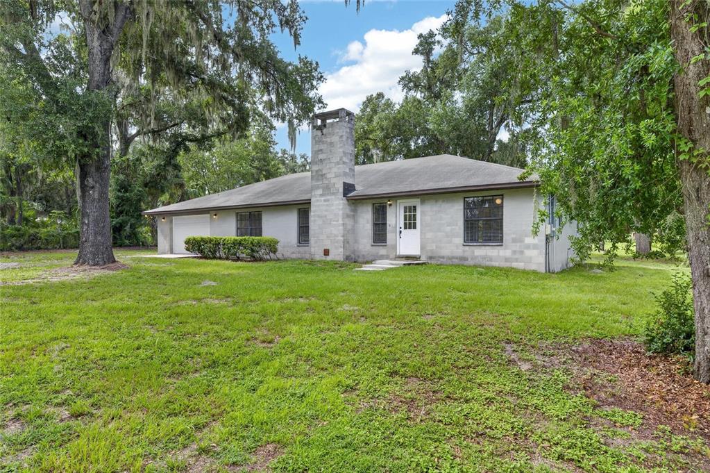 A single-story concrete block house with a chimney and attached garage sits on a lawn — 615 THOMPSON ROAD, LITHIA, FL