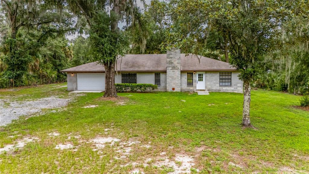 A single-story house with a concrete block exterior, a stone chimney, and a gravel driveway — 615 THOMPSON ROAD, LITHIA, FL