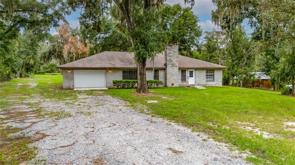 A single-story house with a gravel driveway, stone chimney, and attached garage sits among trees — 615 THOMPSON ROAD, LITHIA, FL