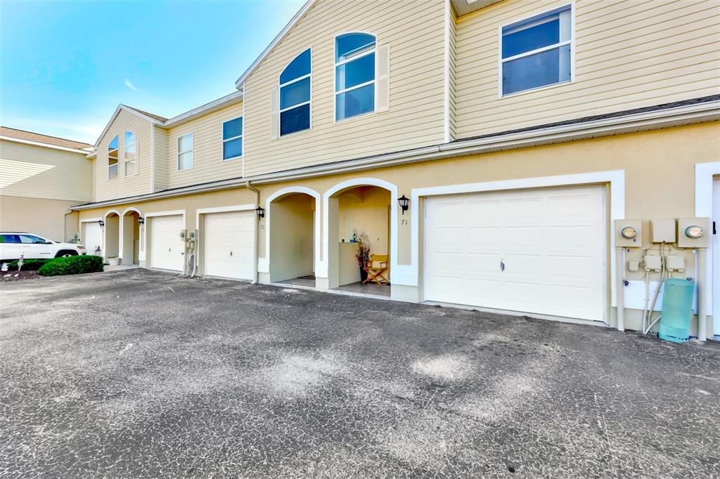 The exterior of a multi-unit townhouse complex features beige siding, white garage doors, and arched entryways — 6400 46TH AVENUE N UNIT 71, KENNETH CITY, FL
