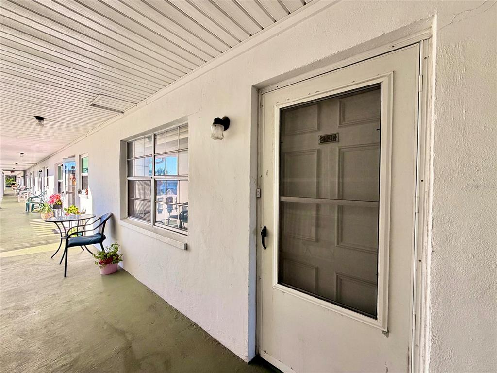 A white exterior door with a screen door leads to a covered outdoor walkway — 4746 AZALEA DRIVE UNIT 213, NEW PORT RICHEY, FL