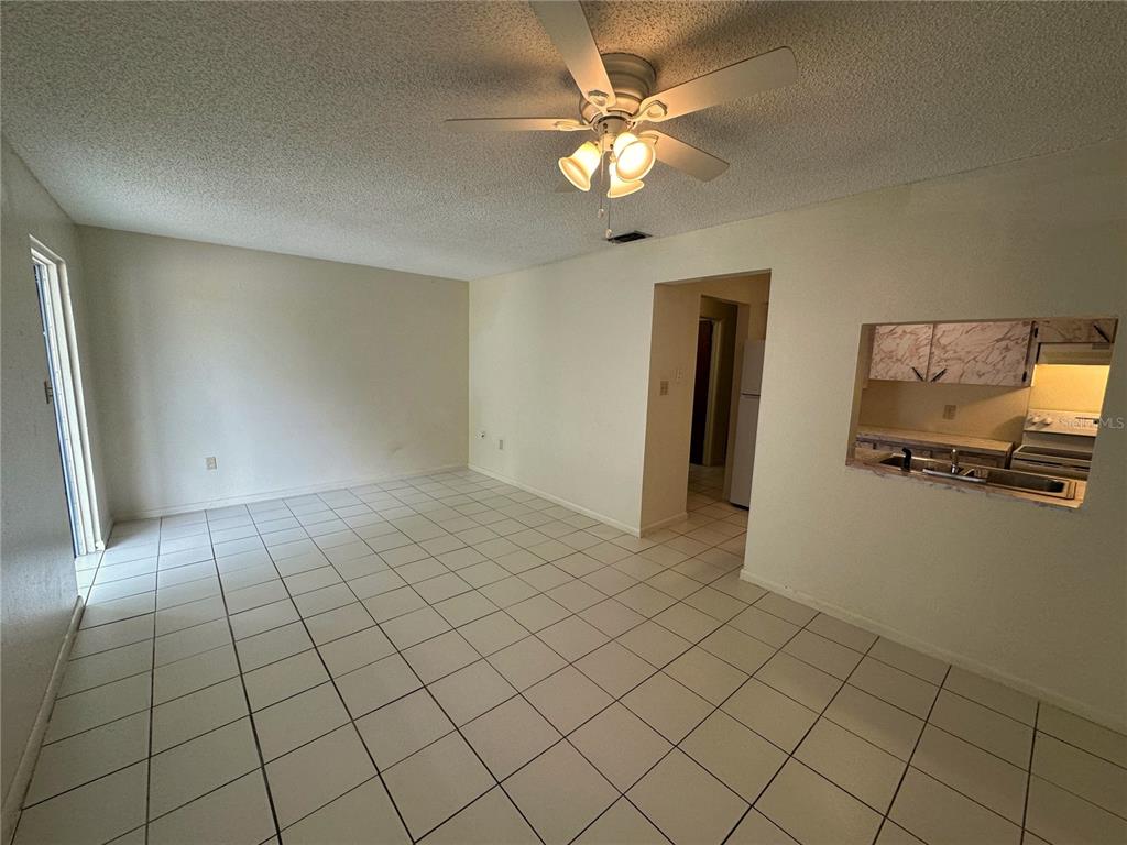 An empty living room features white tile flooring, a ceiling fan, and a kitchen pass-through — 325 N 5TH STREET UNIT 5, HAINES CITY, FL