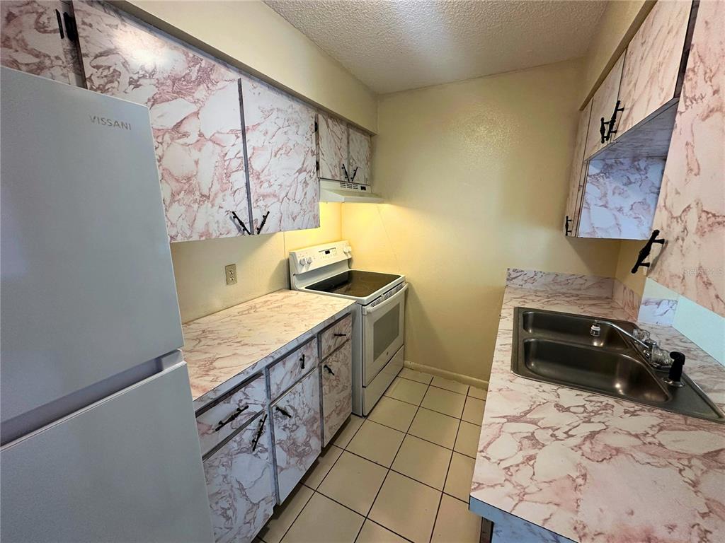A galley kitchen features white appliances and cabinets covered in a pink marble-patterned contact paper — 325 N 5TH STREET UNIT 5, HAINES CITY, FL