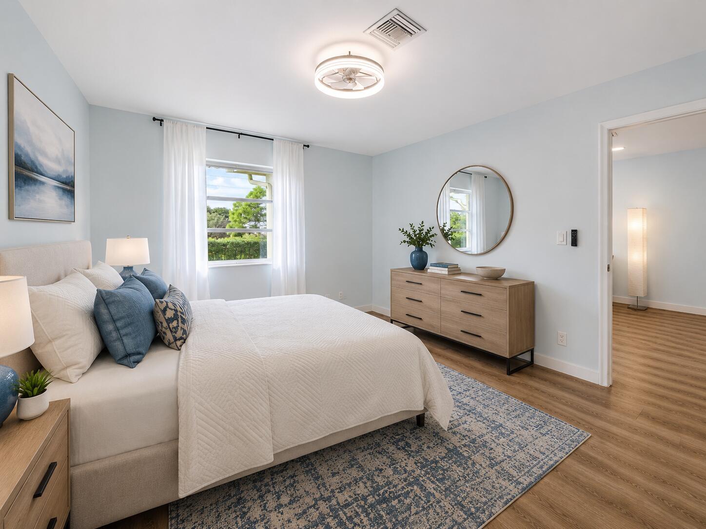 A bedroom features a bed, dresser, circular mirror, and light blue walls with wood flooring — 1101 Cactus Terrace # 203, Delray Beach FL 33445, DELRAY BEACH, FL