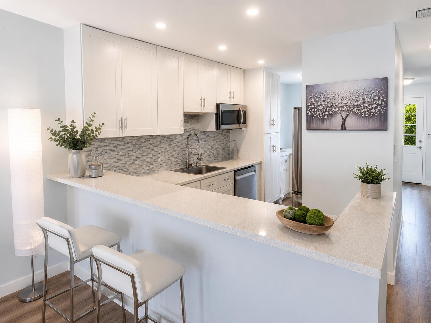 A modern kitchen features white cabinets, quartz countertops, a breakfast bar, and stainless steel appliances — 1101 Cactus Terrace # 203, Delray Beach FL 33445, DELRAY BEACH, FL