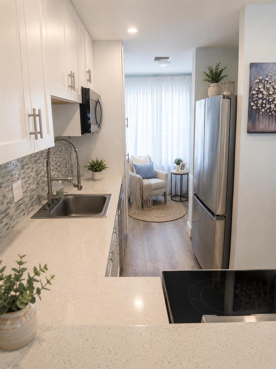 A galley kitchen with white cabinets, stainless steel appliances, and a cozy seating area beyond — 1101 Cactus Terrace # 203, Delray Beach FL 33445, DELRAY BEACH, FL