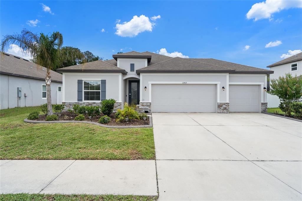 A single-story house with a three-car garage, stone accents, and a landscaped front yard — 12409 BRICK COBBLESTONE DRIVE, RIVERVIEW, FL