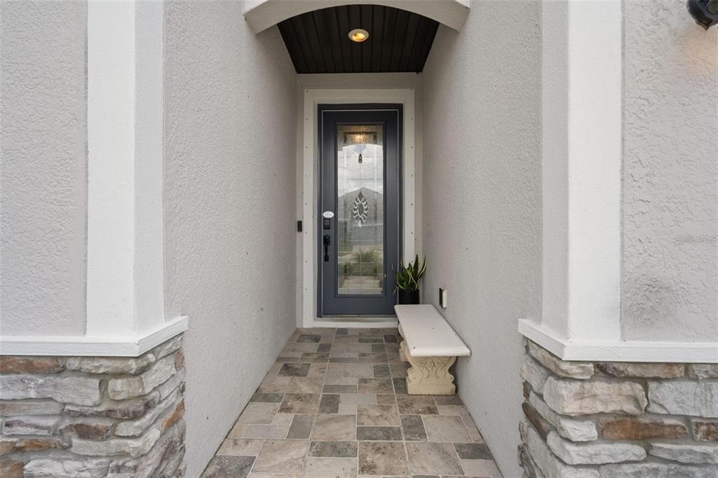 A covered entryway features a gray front door, stone-accented columns, and tiled flooring — 12409 BRICK COBBLESTONE DRIVE, RIVERVIEW, FL