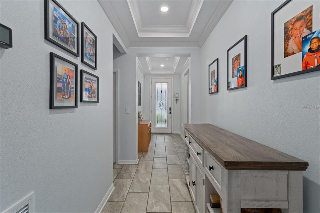 A hallway with light gray walls, tile flooring, a wooden console table, and framed photos — 12409 BRICK COBBLESTONE DRIVE, RIVERVIEW, FL