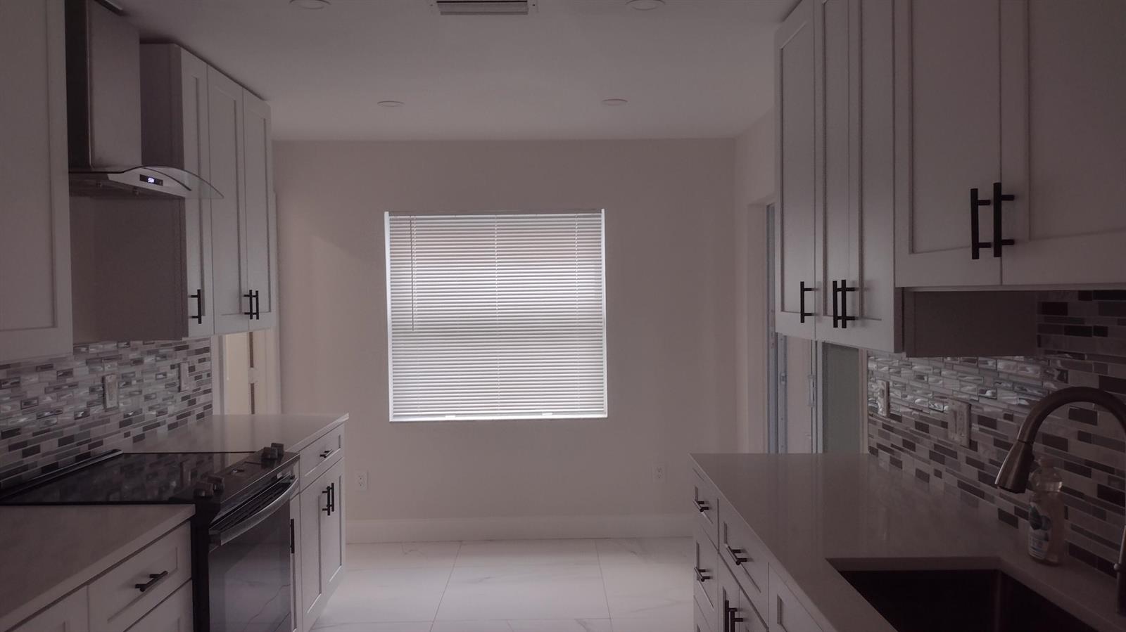 A modern kitchen features white cabinets, a tiled backsplash, stainless steel appliances, and tile flooring — 22682 SW 65th Circle, Boca Raton FL 33428, BOCA RATON, FL