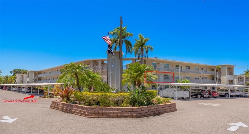 Exterior view of a multi-story apartment building with covered parking spaces and palm trees — 948 VIRGINIA STREET UNIT 207, DUNEDIN, FL