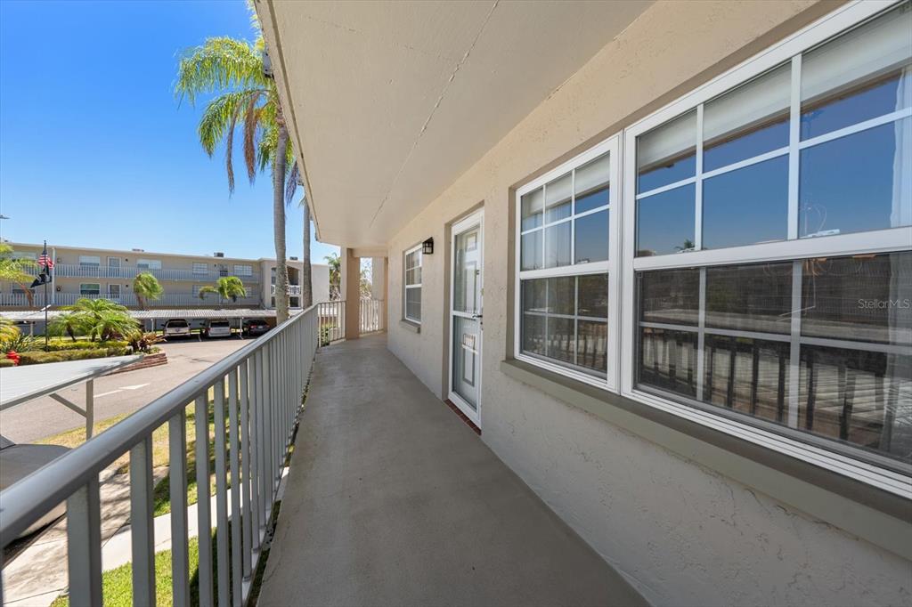 An outdoor walkway with a metal railing overlooks a parking lot and palm trees — 948 VIRGINIA STREET UNIT 207, DUNEDIN, FL