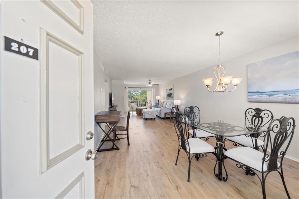 An open-concept living and dining area features wood-look flooring and a glass-topped dining table — 948 VIRGINIA STREET UNIT 207, DUNEDIN, FL
