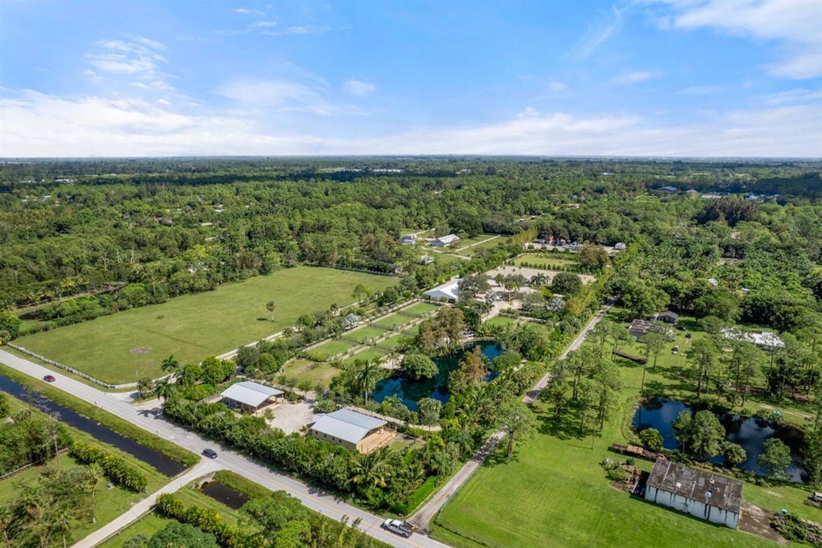 An aerial view shows a rural property with multiple buildings, a pond, and large pastures — 1754 B Road, FL 33470, FL