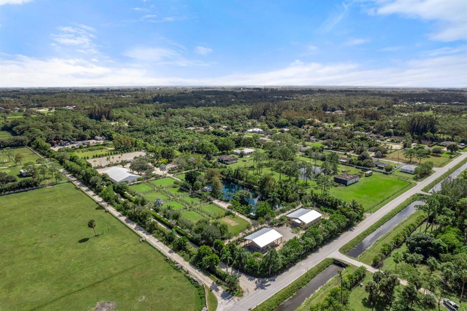 An aerial view shows a rural property with multiple buildings, a pond, and fenced pastures — 1754 B Road, FL 33470, FL