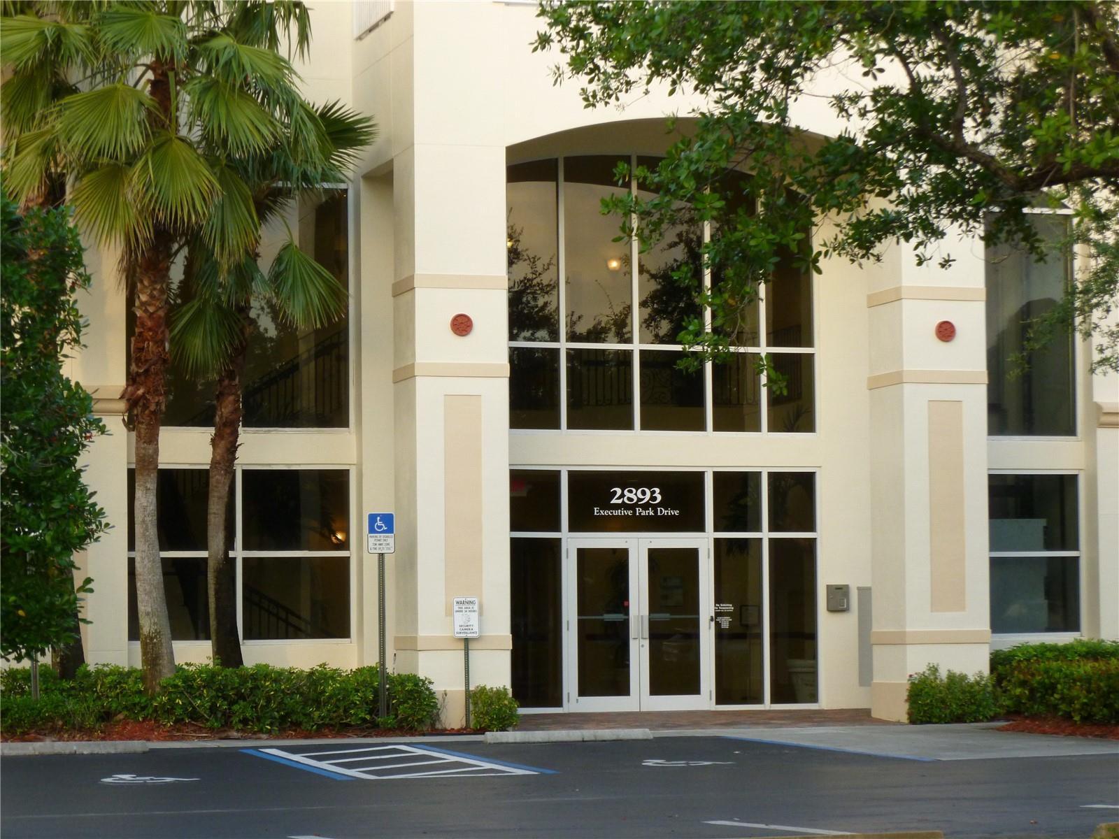 The exterior of a multi-story commercial building features a glass entrance and palm trees — 2893 Executive Park Drive # 105, Weston FL 33331, WESTON, FL