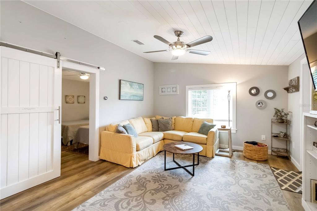 A living room features a yellow sectional sofa, a ceiling fan, and a sliding barn door — 2537 ASHTON ROAD, SARASOTA, FL