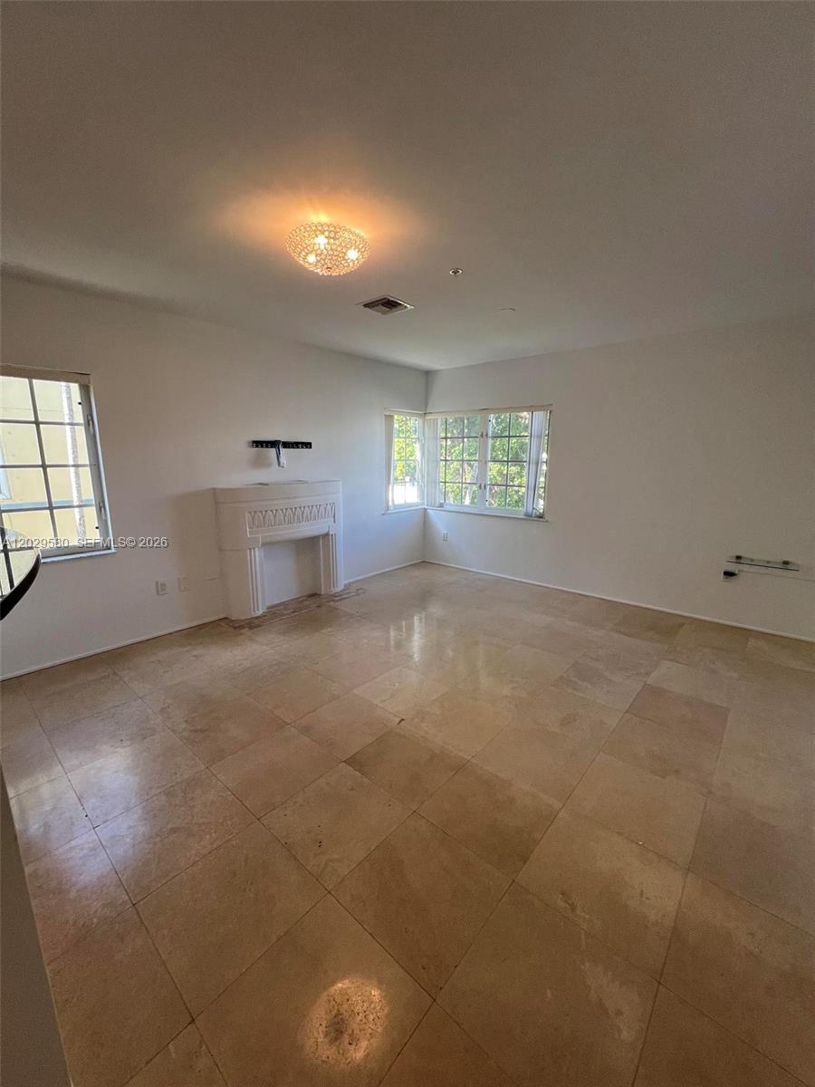 An empty living room features a white fireplace, tile flooring, and windows on two walls — 600 Euclid Ave # 5A, Miami Beach FL 33139, MIAMI BEACH, FL