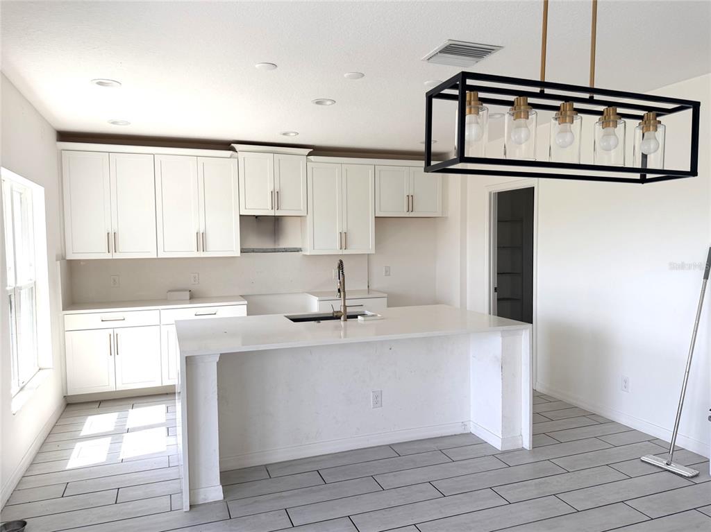 A kitchen features white cabinets, a central island with a sink, and a rectangular pendant light — 269 HAMLET LOOP, DAVENPORT, FL