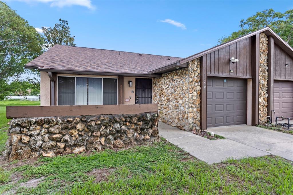 A single-story house features a stone facade, a brown garage door, and a front lawn — 5781 SHALE COURT, WINTER PARK, FL