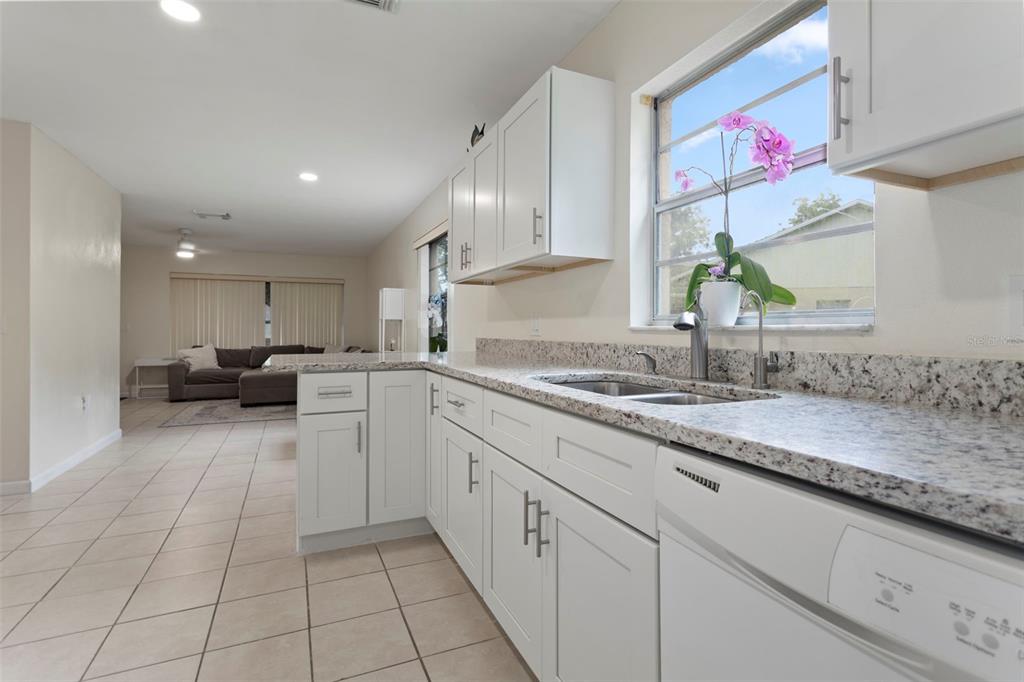 A kitchen with white cabinets, granite countertops, and tile flooring overlooks an adjacent living area — 5781 SHALE COURT, WINTER PARK, FL