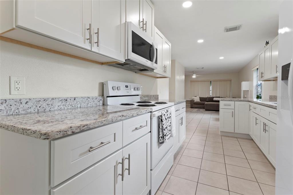 A white kitchen features granite countertops, white cabinets, and white appliances, opening into a living area — 5781 SHALE COURT, WINTER PARK, FL
