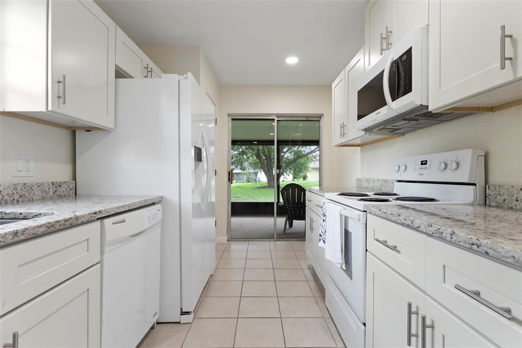 A galley kitchen features white cabinets, granite countertops, white appliances, and a sliding glass door — 5781 SHALE COURT, WINTER PARK, FL