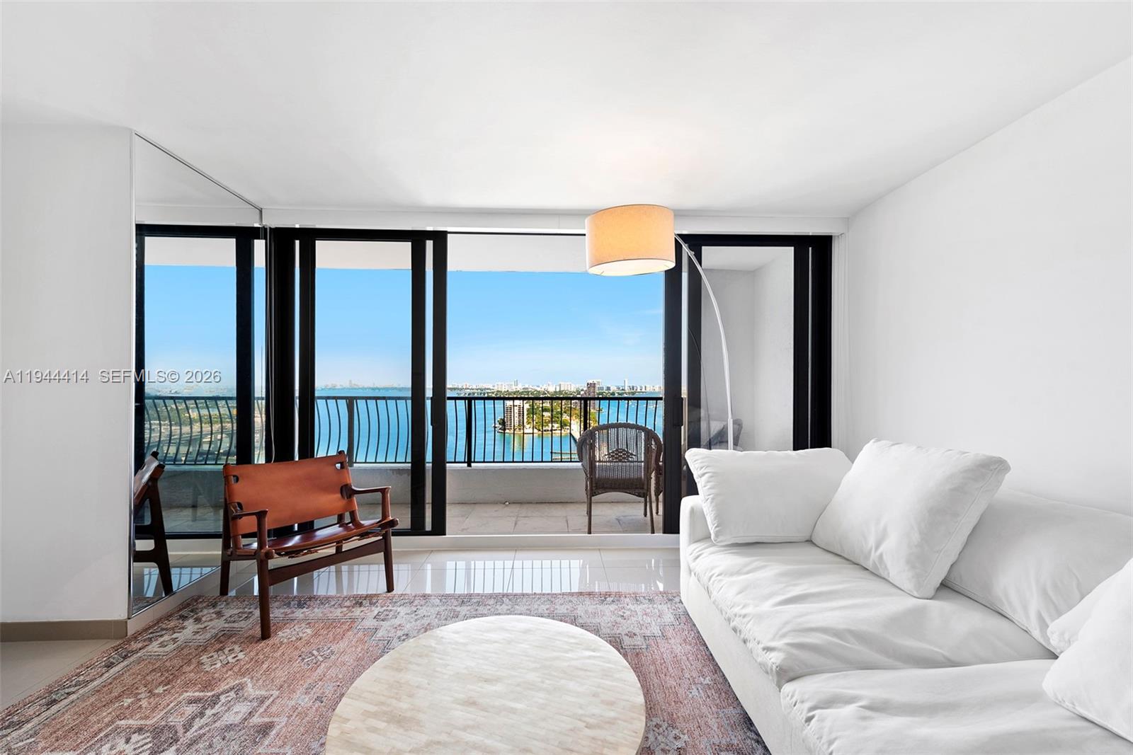 A living room features a white sofa, a leather chair, and a balcony overlooking water — 555 NE 15th St # 26B, Miami FL 33132, MIAMI, FL