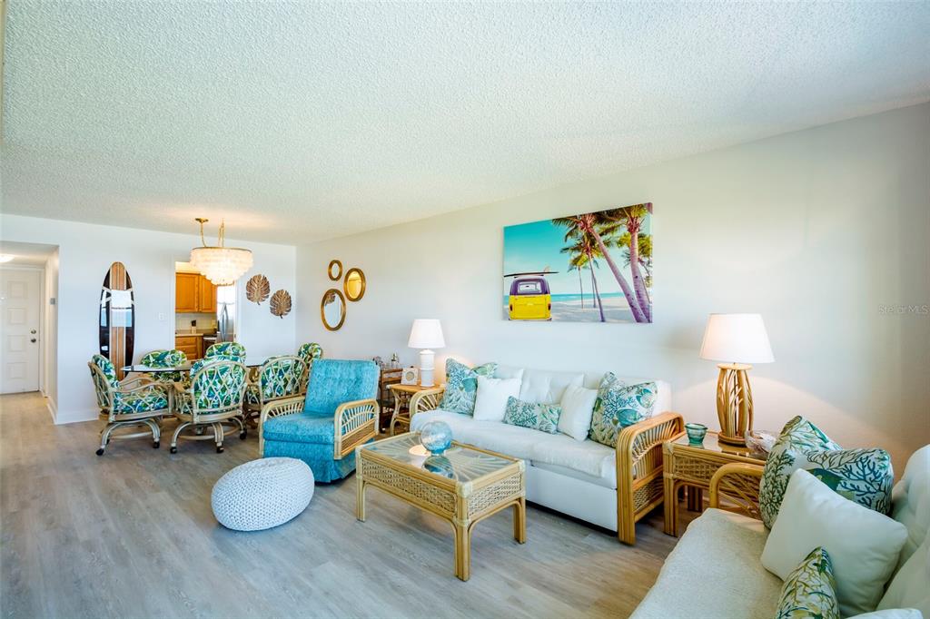 A living and dining area features light wood-look flooring, wicker furniture, and coastal-themed decor — 1230 GULF BOULEVARD UNIT 903, CLEARWATER BEACH, FL