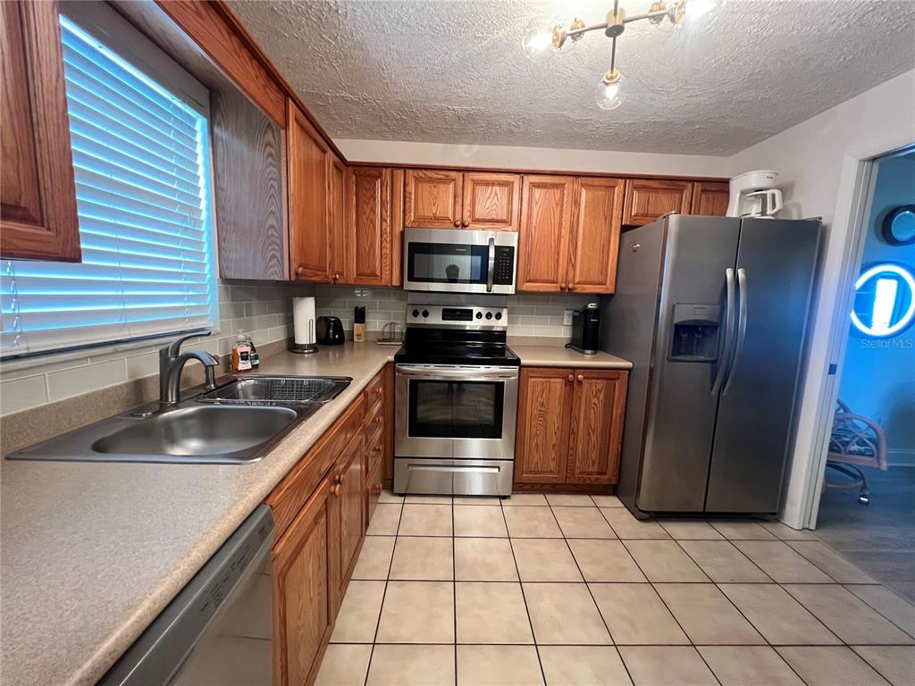 A kitchen features wood cabinets, stainless steel appliances, a double sink, and tiled flooring — 1230 GULF BOULEVARD UNIT 903, CLEARWATER BEACH, FL