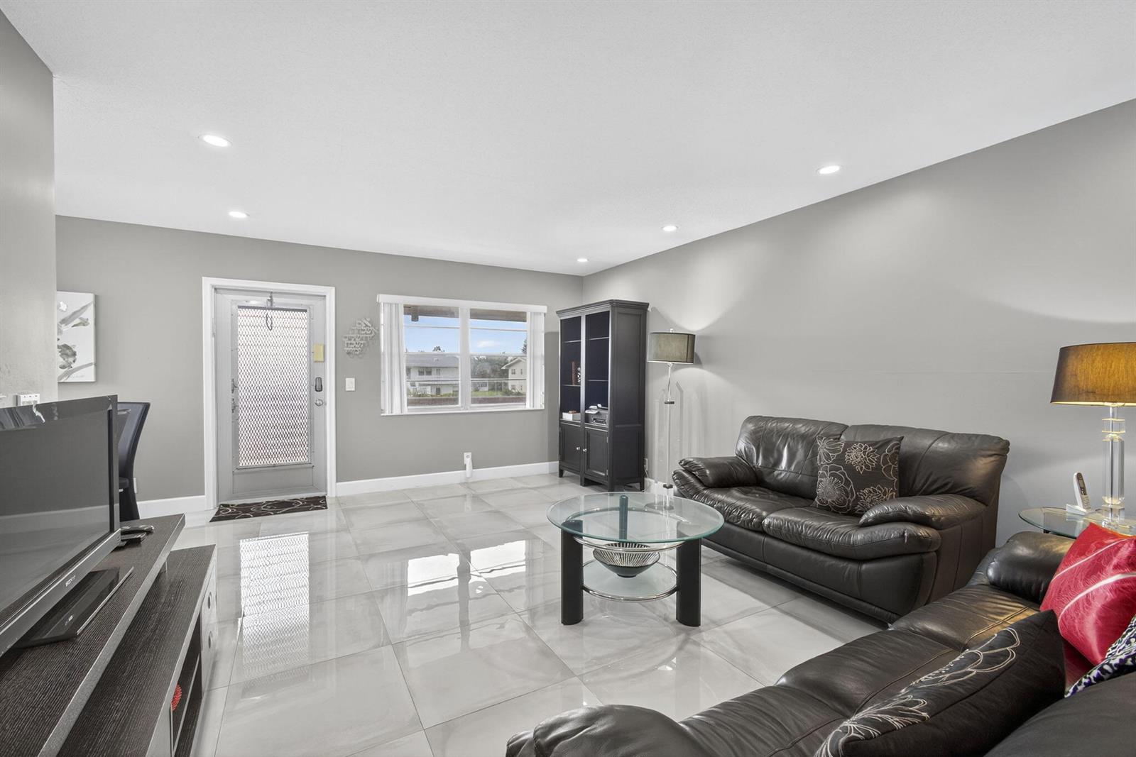 A living room features gray walls, large light-colored floor tiles, and black leather furniture — 160 Easthampton G, West Palm Beach FL 33417, WEST PALM BEACH, FL