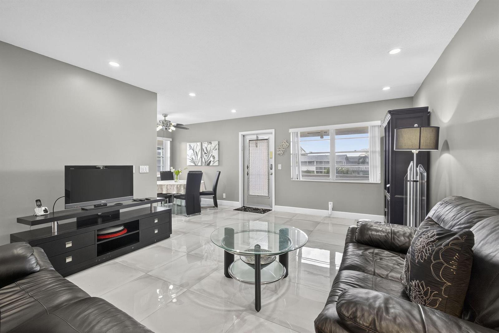A living room features gray walls, large light-colored floor tiles, and black leather furniture — 160 Easthampton G, West Palm Beach FL 33417, WEST PALM BEACH, FL