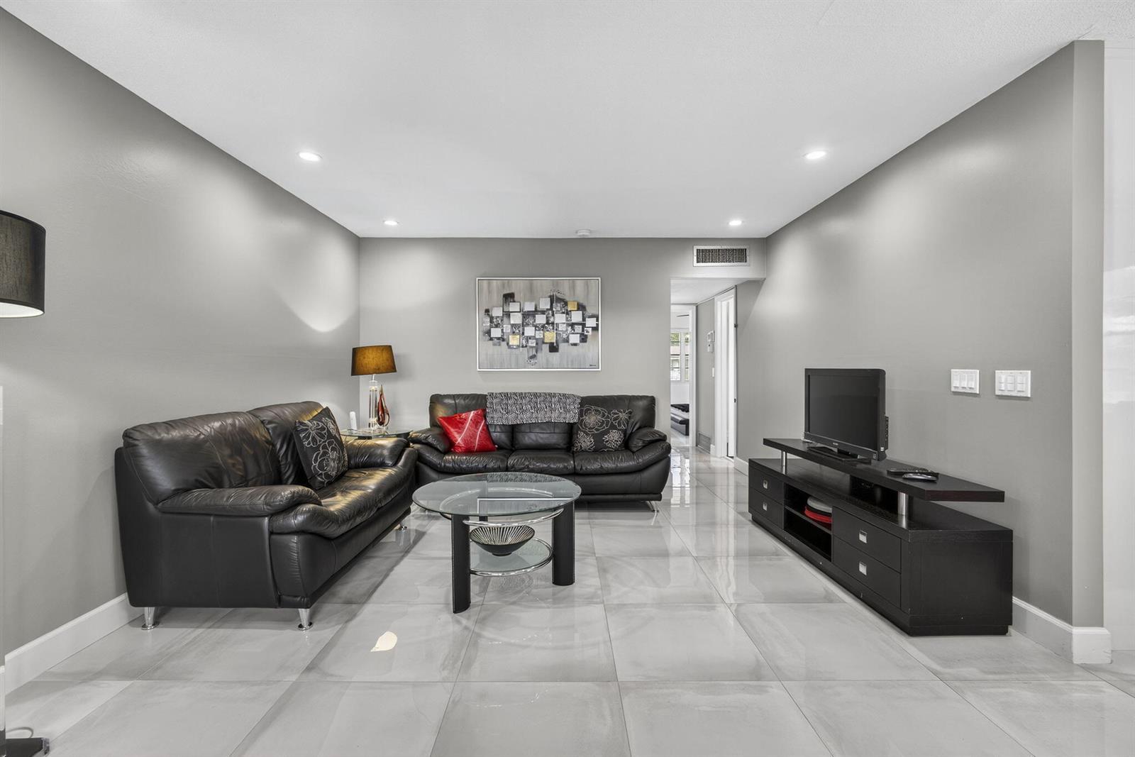 A living room features gray walls, large light-colored floor tiles, and black leather furniture — 160 Easthampton G, West Palm Beach FL 33417, WEST PALM BEACH, FL