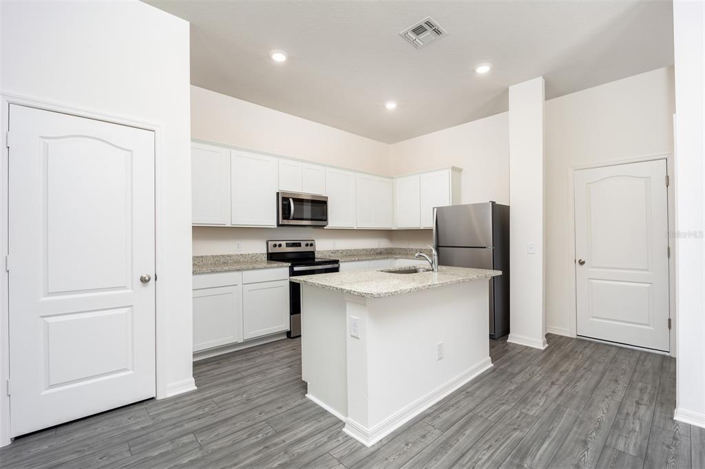 A kitchen features white cabinets, granite countertops, stainless steel appliances, and gray wood-look flooring — 643 POPPY LANE, DUNDEE, FL