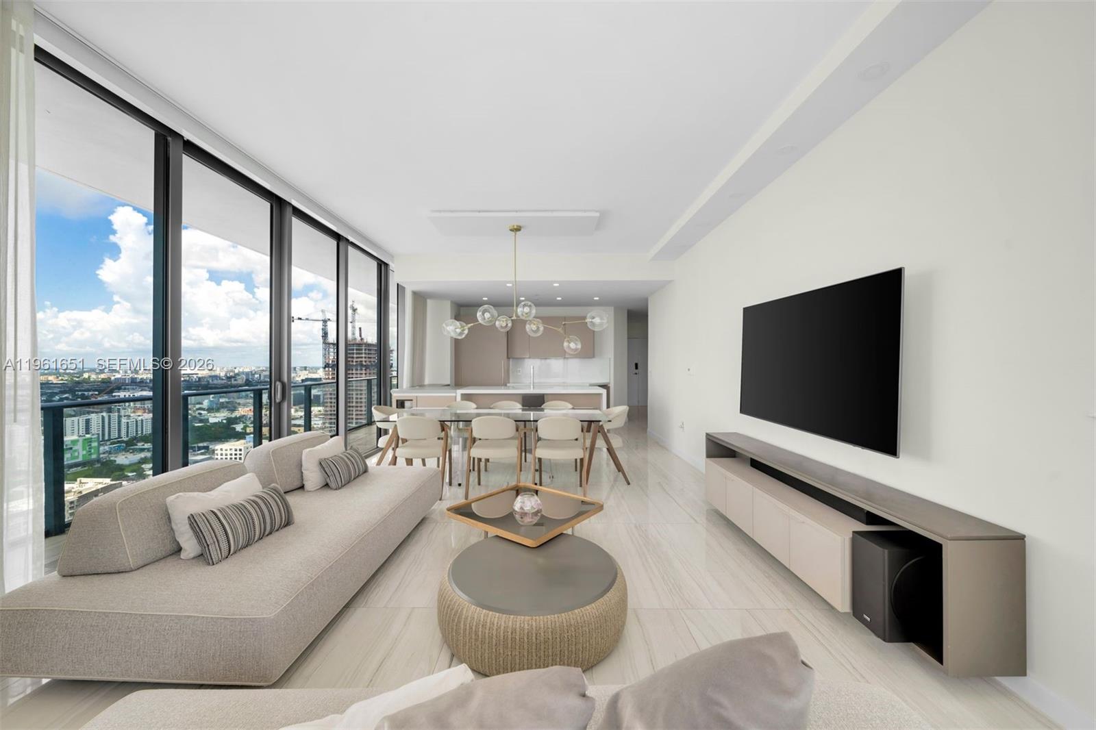 A modern living and dining area features floor-to-ceiling windows, light tile flooring, and city views — 480 NE 31st St # 3401, Miami FL 33137, MIAMI, FL