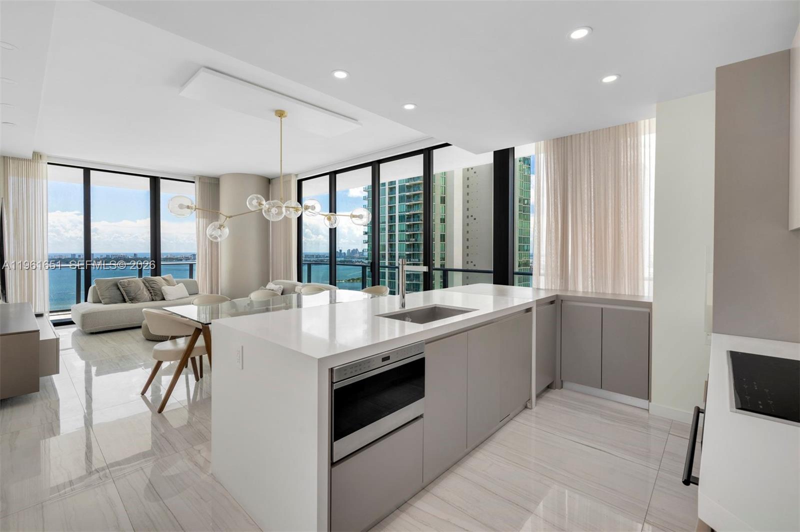 A modern kitchen island with a built-in microwave faces a dining area with floor-to-ceiling windows — 480 NE 31st St # 3401, Miami FL 33137, MIAMI, FL