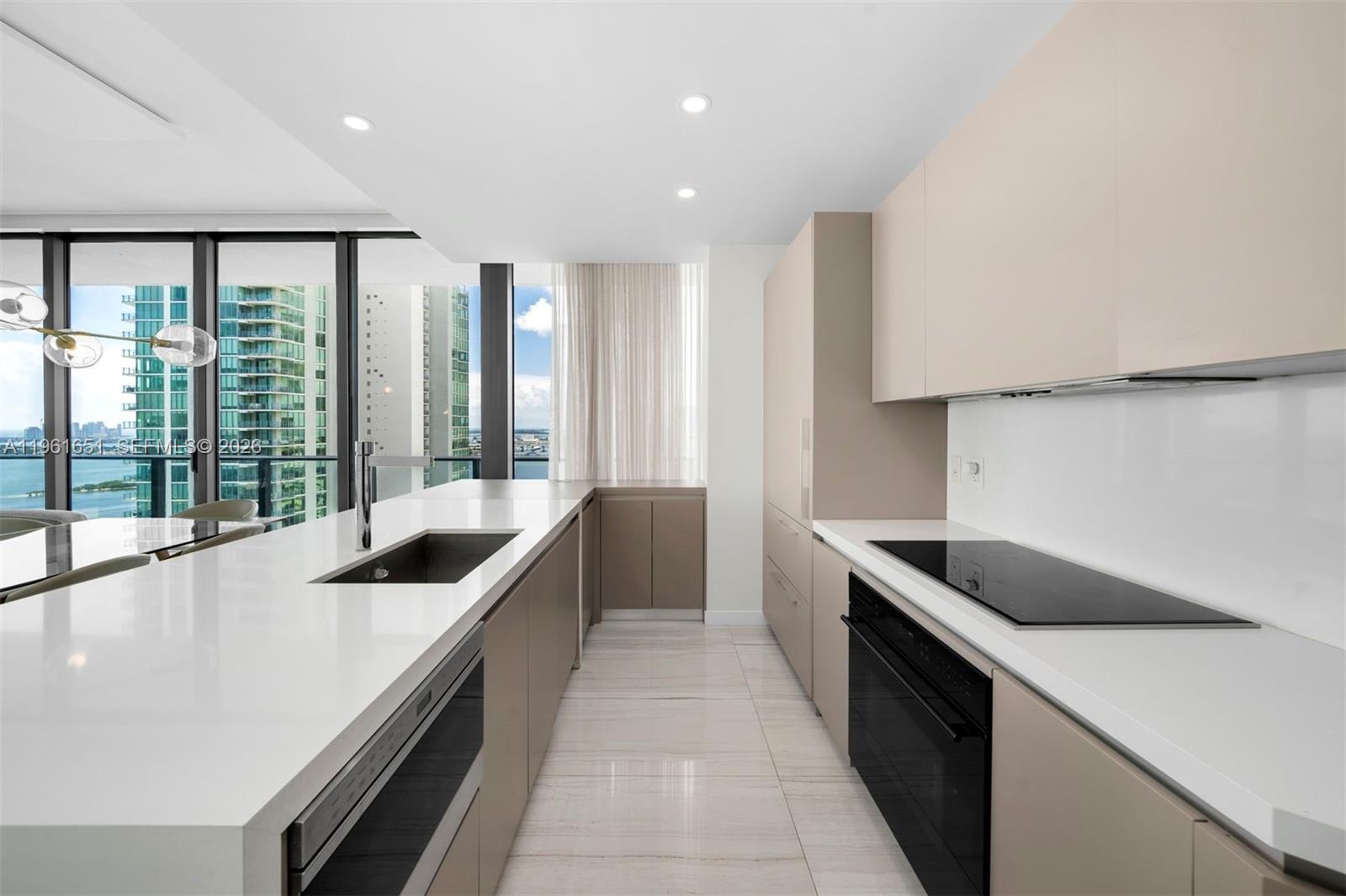 A modern kitchen features light-toned cabinetry, white countertops, a central island, and floor-to-ceiling windows — 480 NE 31st St # 3401, Miami FL 33137, MIAMI, FL